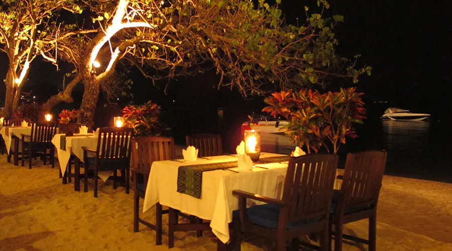 Beach tables with white cloths under a lit tree at night