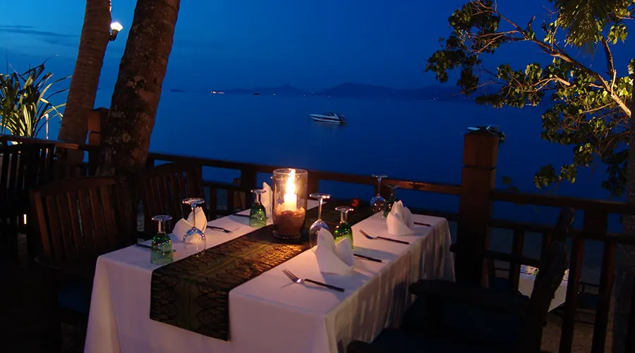 A candlelit table by the rail at blue hour, the sea and islands beyond