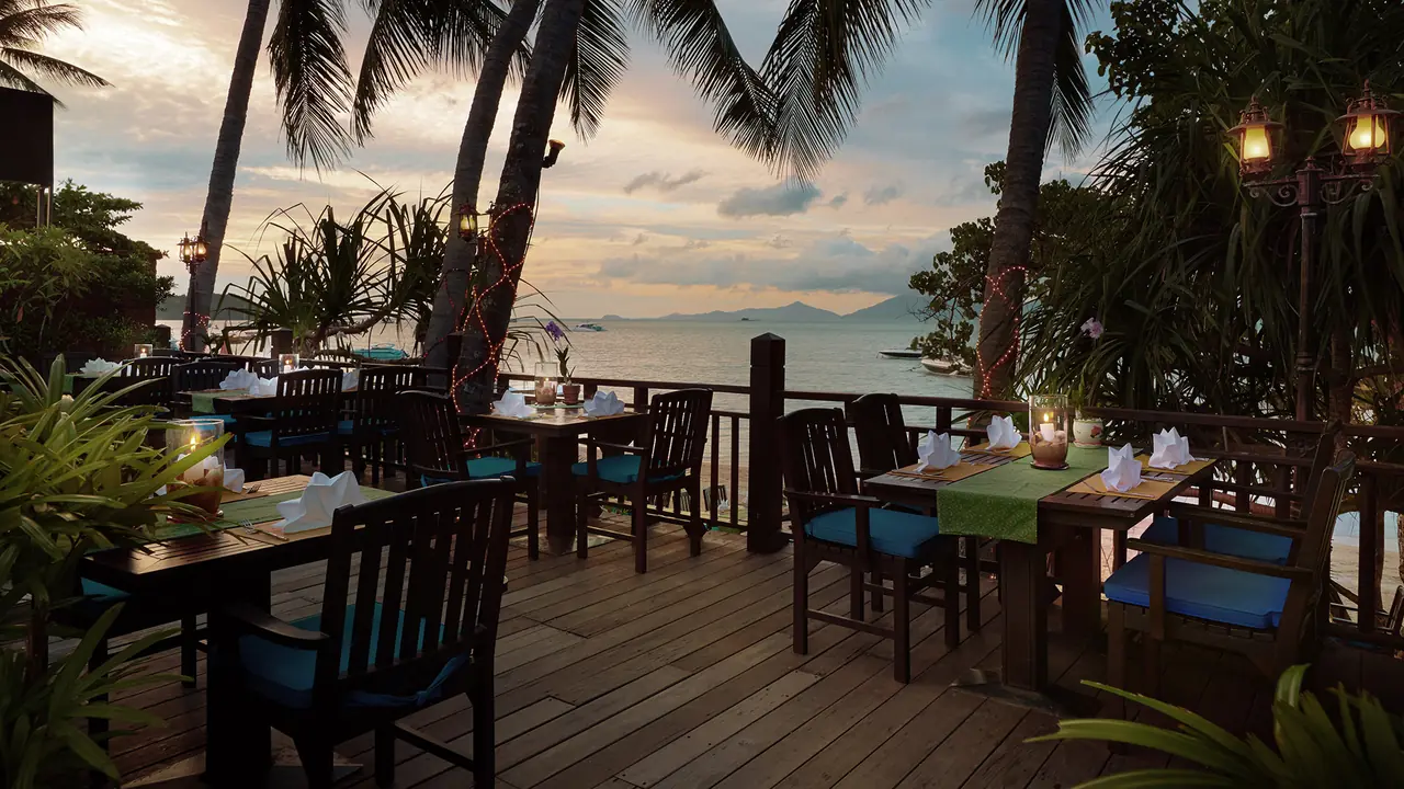 Wooden deck tables with blue cushions, the sea and palms at sunset