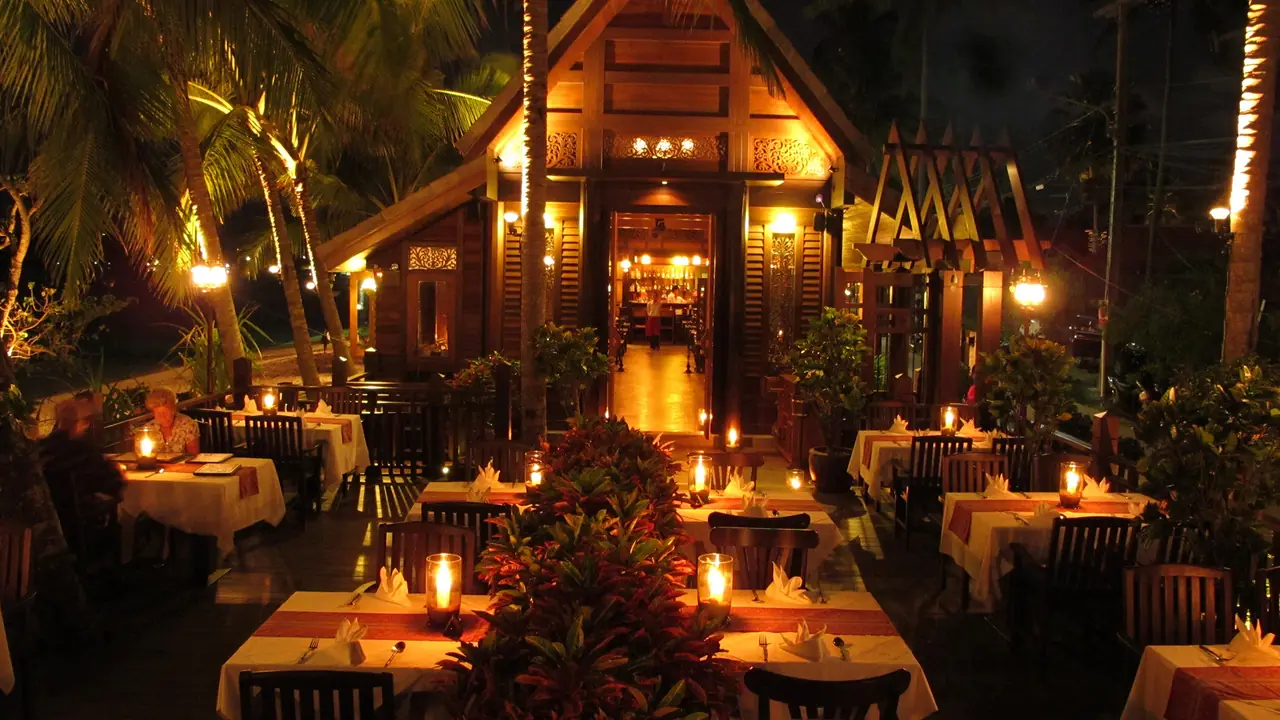 The carved Thai house at night, candlelit tables in the tropical garden