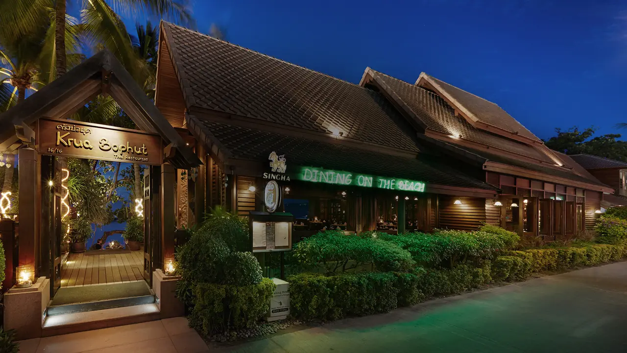 The teak Thai house from the street at blue hour, lit sign and garden