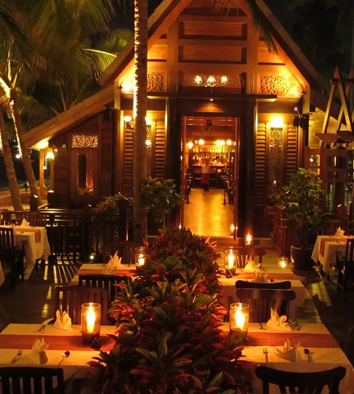 The carved Thai house at night, candlelit tables in the tropical garden
