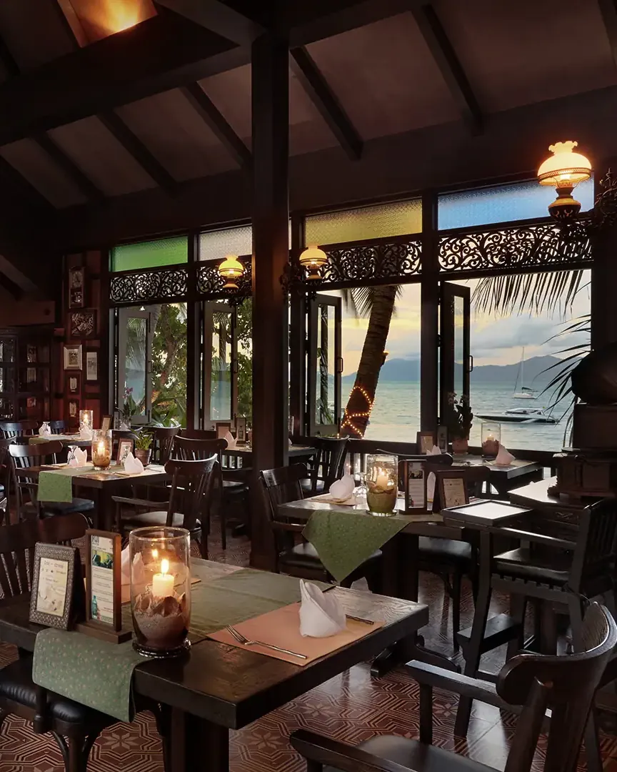 Inside the teak hall by day, lanterns, carved windows onto the beach