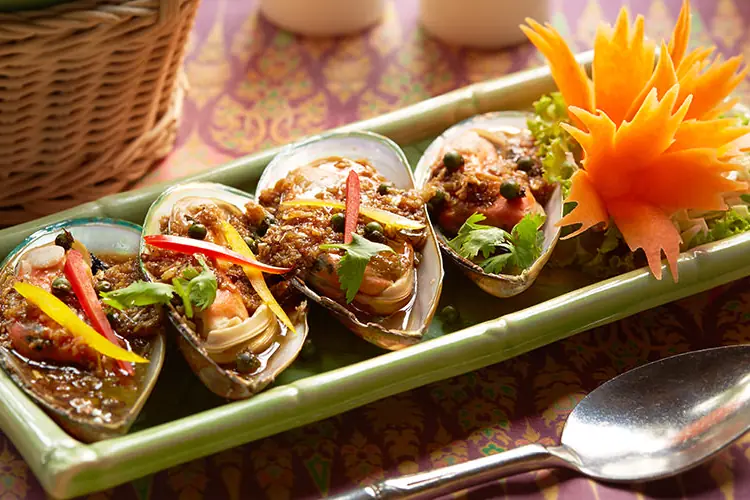Mussels in their shells with chilli and herbs on a long green plate, with a carved carrot flower