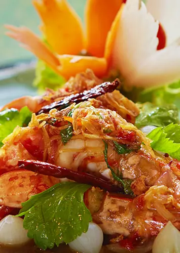Prawns in a red chilli sauce with coriander, a carved white vegetable swan behind
